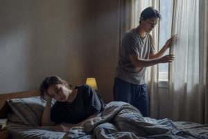 Aidant ouvre rideaux et encourage proche dépressif à se lever du lit en journée.