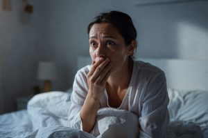 Femme se réveillant surprise dans son lit moderne, main sur la bouche.