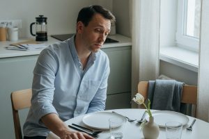 Homme seul à table face à chaise vide dans cuisine lumineuse