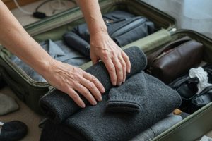 Mains repliant un pull dans une valise ouverte au sol