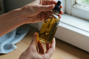 Mains tenant une petite bouteille d'huile de CBD devant une fenêtre