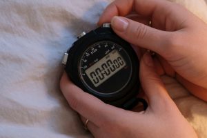 Mains actionnant un chronomètre près de draps froissés à la lumière tamisée.